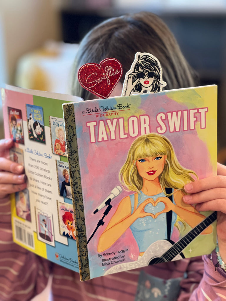 Girl is shown reading a book about Taylor Swift using a Clip Chicks Tay;or Swift themed novelty paper clip as a whimsical bookmark.