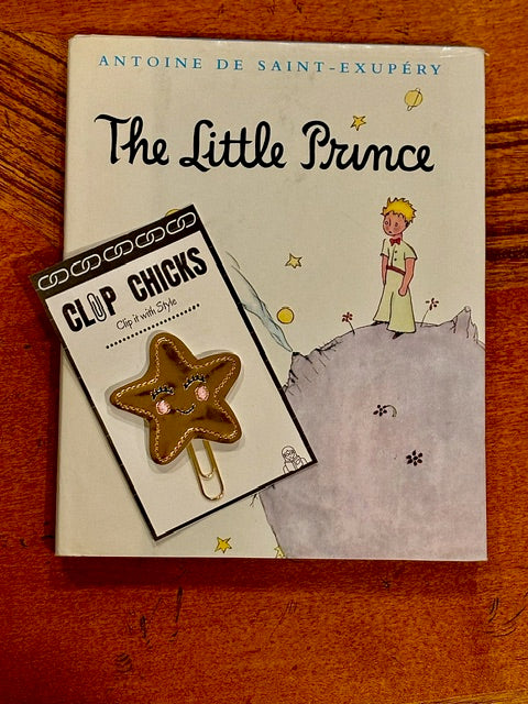 The book, The Little Prince is shown sitting on a table ready to be read with the Smiling Star Clip Chicks in its package laying on the book, ready to be used as a bookmark.