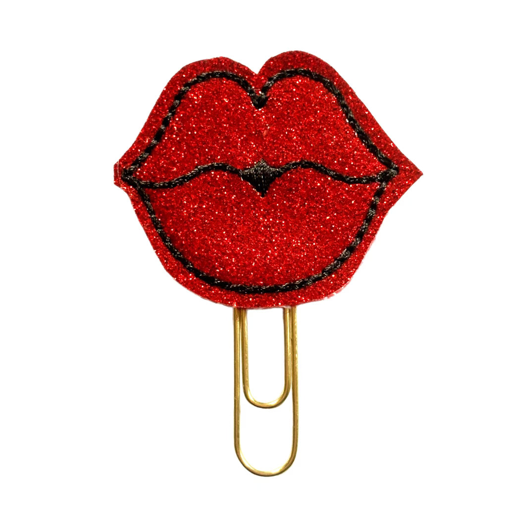 The novelty paper clip is a feltie of red glitter vinyl shaped like lips and embroidered with black stitching, then attached to a gold toned paper clip.