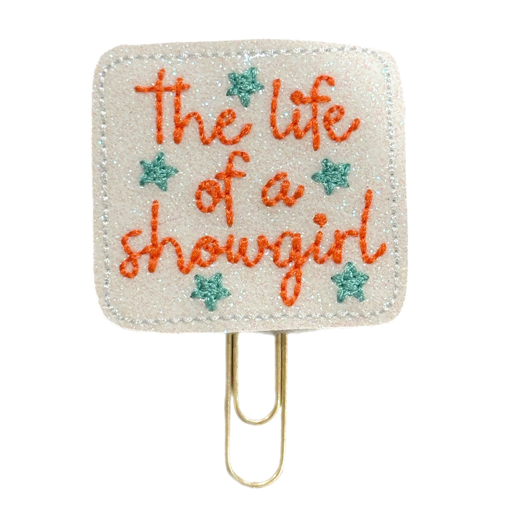 Square paper clip with 'The life of a showgirl' text and star decorations on a white background - a novelty paper clip for Taylor Swift fans by Clip Chicks LLC.