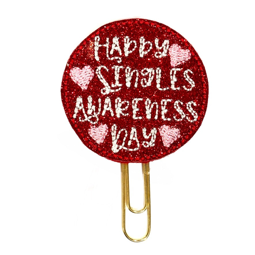 Happy Singles Awareness Day is embroidered on a red glittery circular vinyl feltie, then attached to a gold toned paper clip.