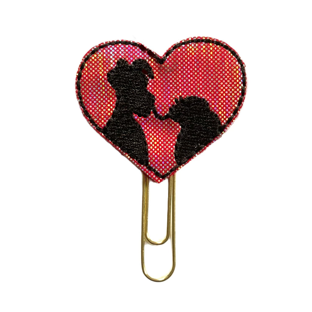 A novelty paper clip with a red shimmery vinyl feltie in the shape of a heart with the silhouette of Lady and the Tramp eating spaghetti  embroidered in black onto the feltie.