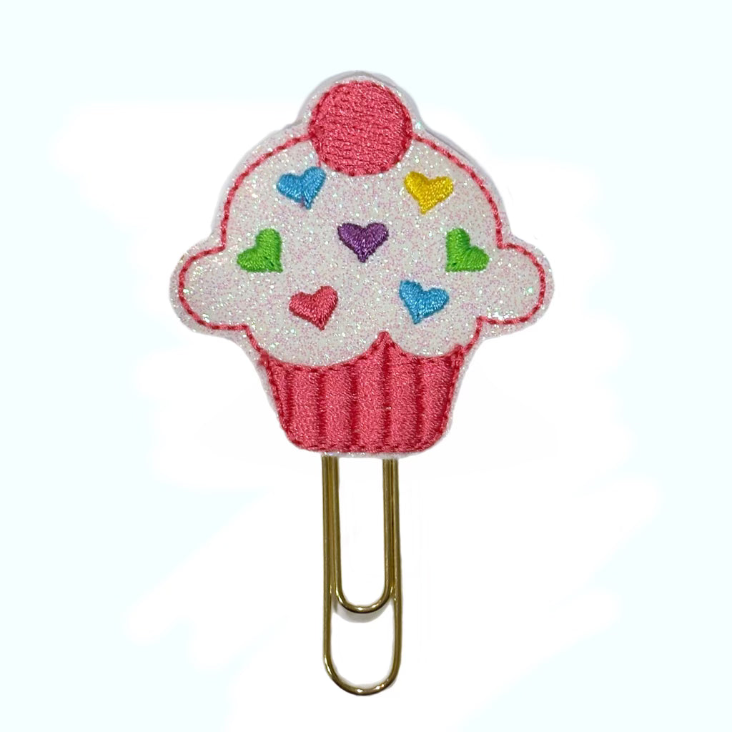 A novelty paper clip shaped like a cupcake with multi colored heart shaped sprinkles embroidered onto a feltie attached to the paper clip.