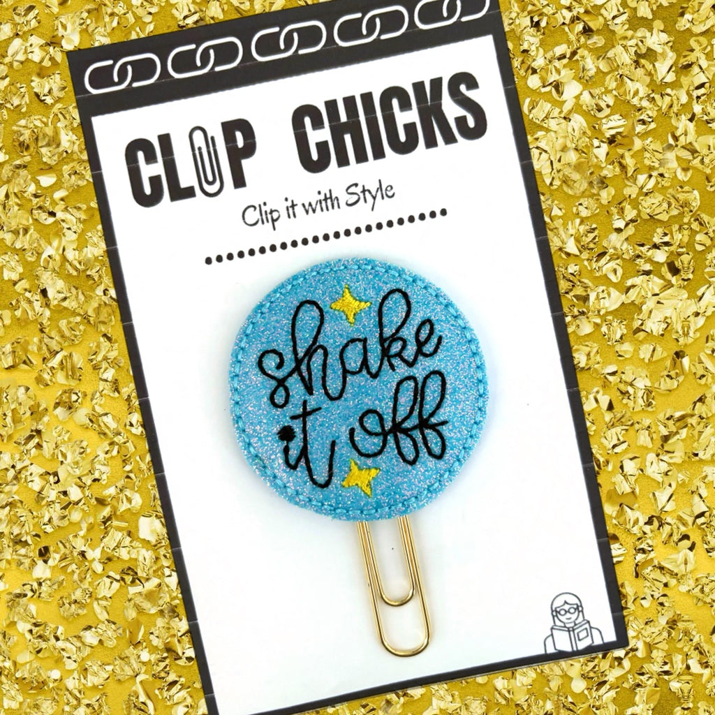 Taylor Swift inspired Shake It Off novelty paper clip from Clip Chicks is shown in its package against a glittery gold background.