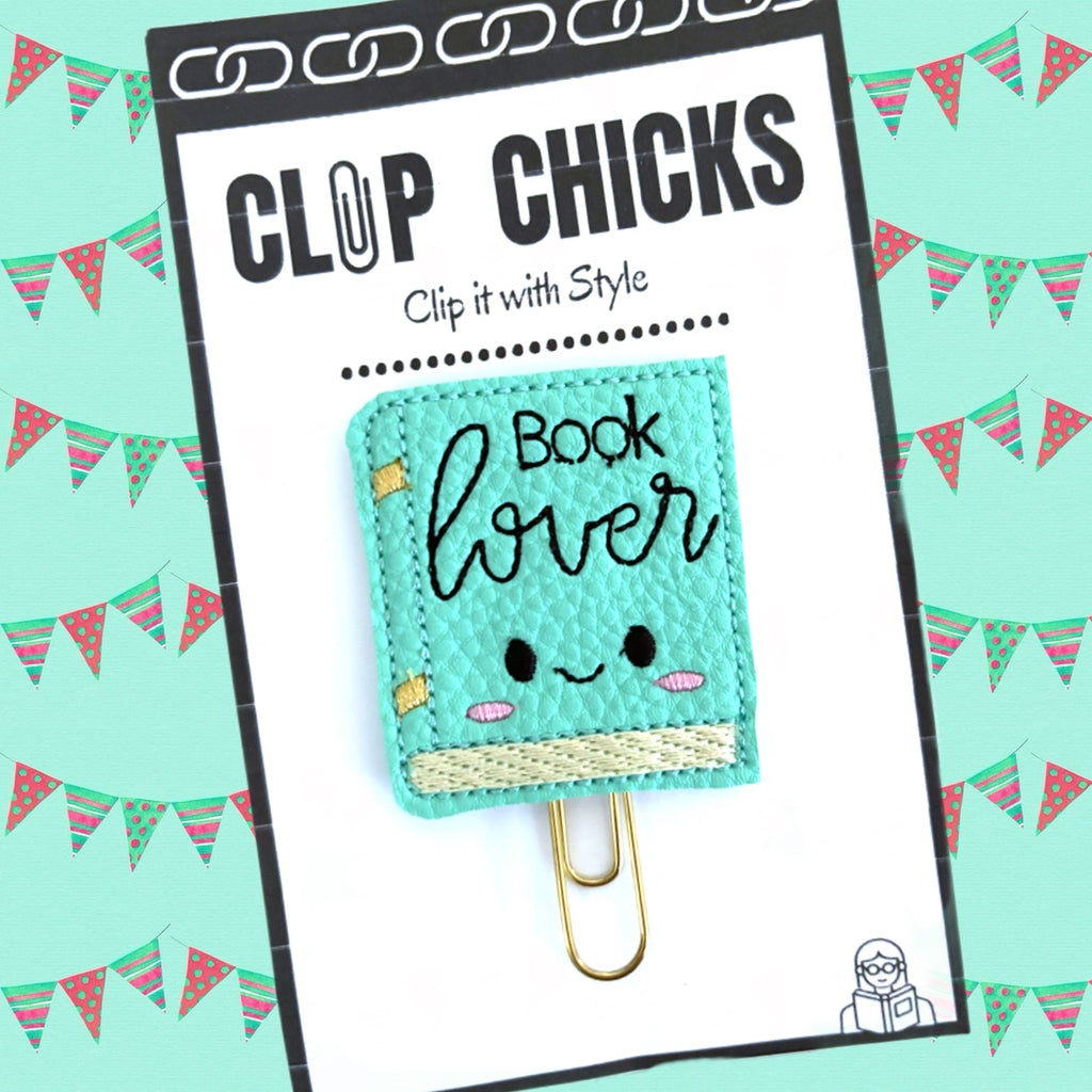 Clip Chicks Book Lover novelty paper clip is shown in its package against a teal background with flags.