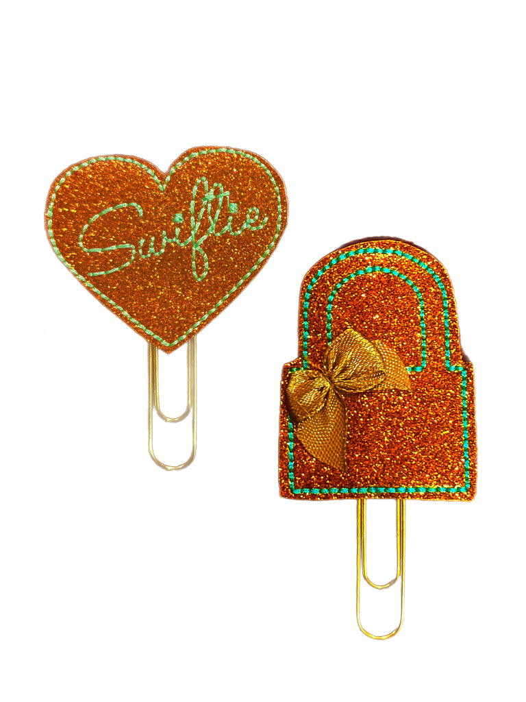Two glittery paper clips, one heart-shaped and one resembling a popsicle, on a white background.