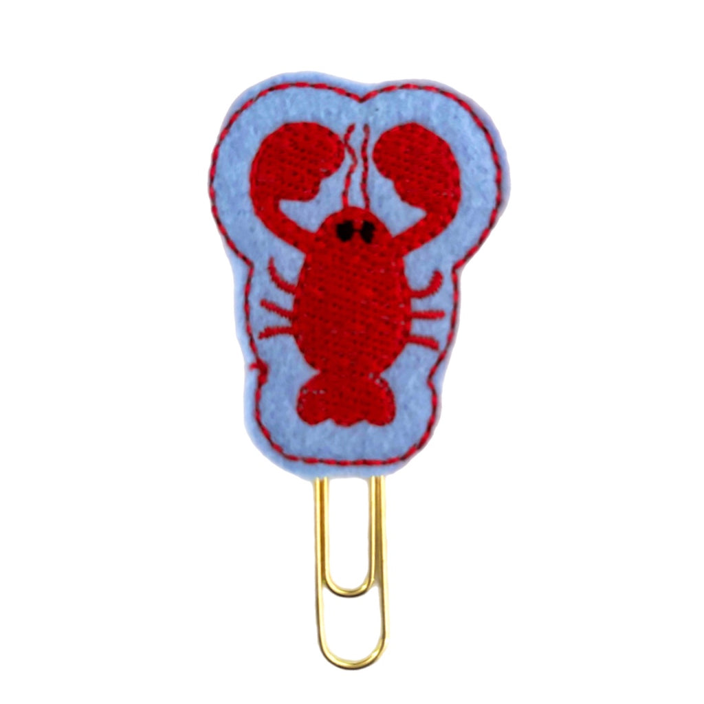 Lobster novelty paper clip from Clip Chicks, shaped like a red lobster with big claws, set on a blue felt background before being attached to a paper clip.