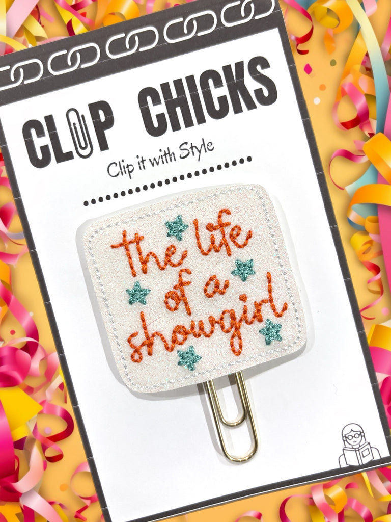 Planner clip with 'The life of a showgirl' text on a colorful background, featuring the brand 'Clip Chicks'. This novelty paper clip from Clip Chicks LLC is a great gift for Taylor Swift fans.