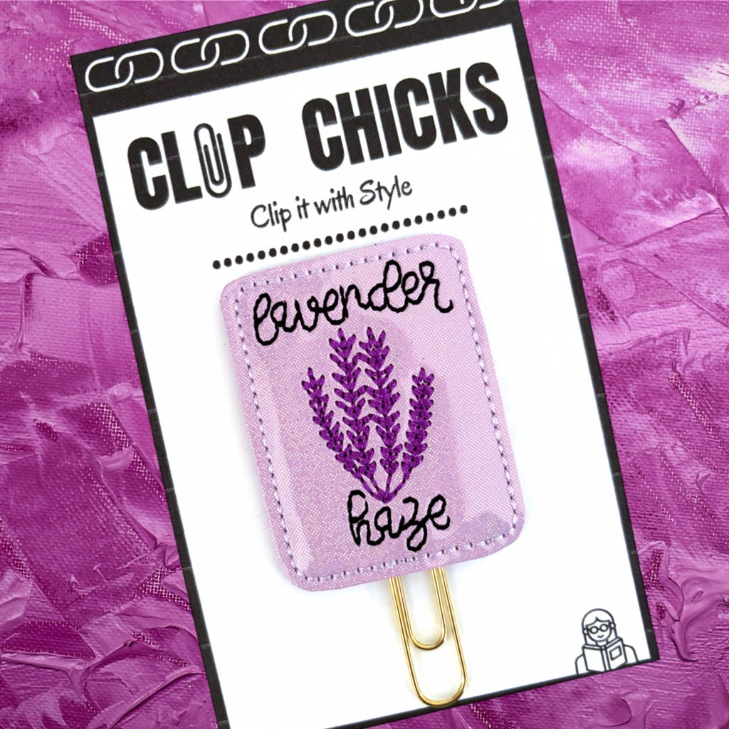 Lavender Haze novelty paper clip from Clip Chicks is shown in its packaging against a dark lavender background.