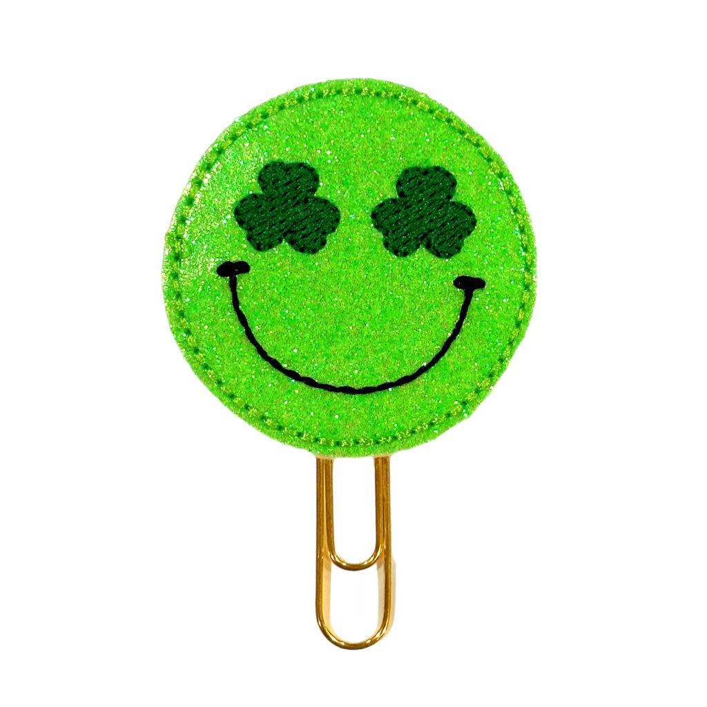 A Clip Chicks novelty paper clip shaped in a circle with a green shimmery happy face where the eyes are shamrocks.