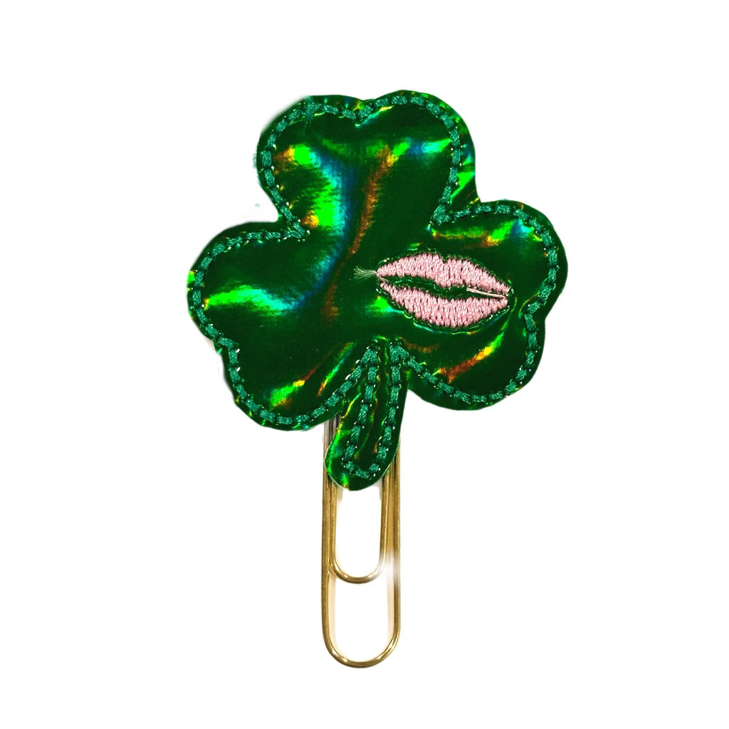 A Clip Chicks novelty paper clip shaped like a shamrock with pink lips embroidered on it.