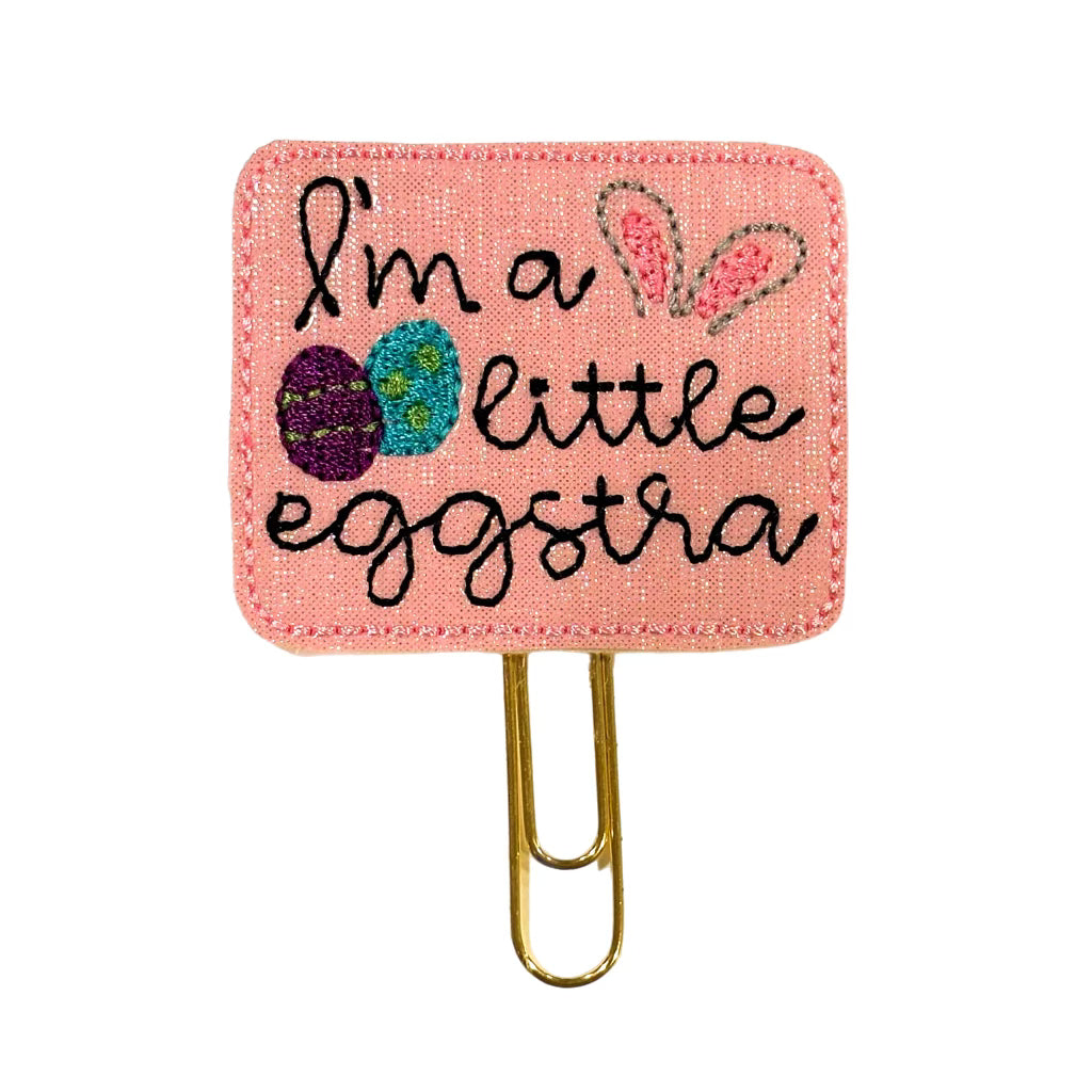 A Clip Chicks novelty paper clip that says I'm a little eggstra and has eggs and bunny ears embroidered on it.