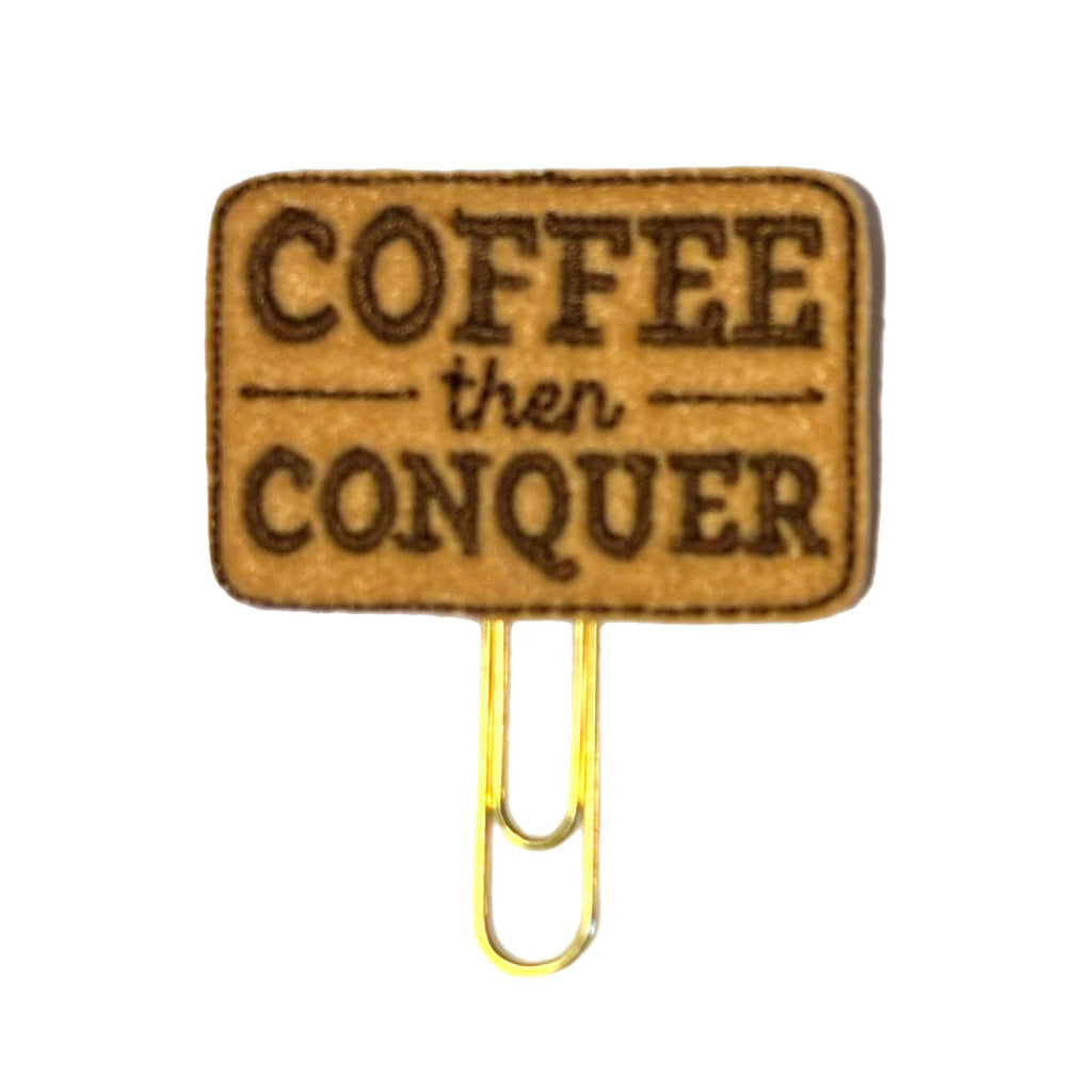 a tan piece of felt is embroidered with dark brown thread the words, Coffee Then Conquer" and attached to a gold toned paper clip to be used as a bookmark or planner clip from Clip Chicks LLC.