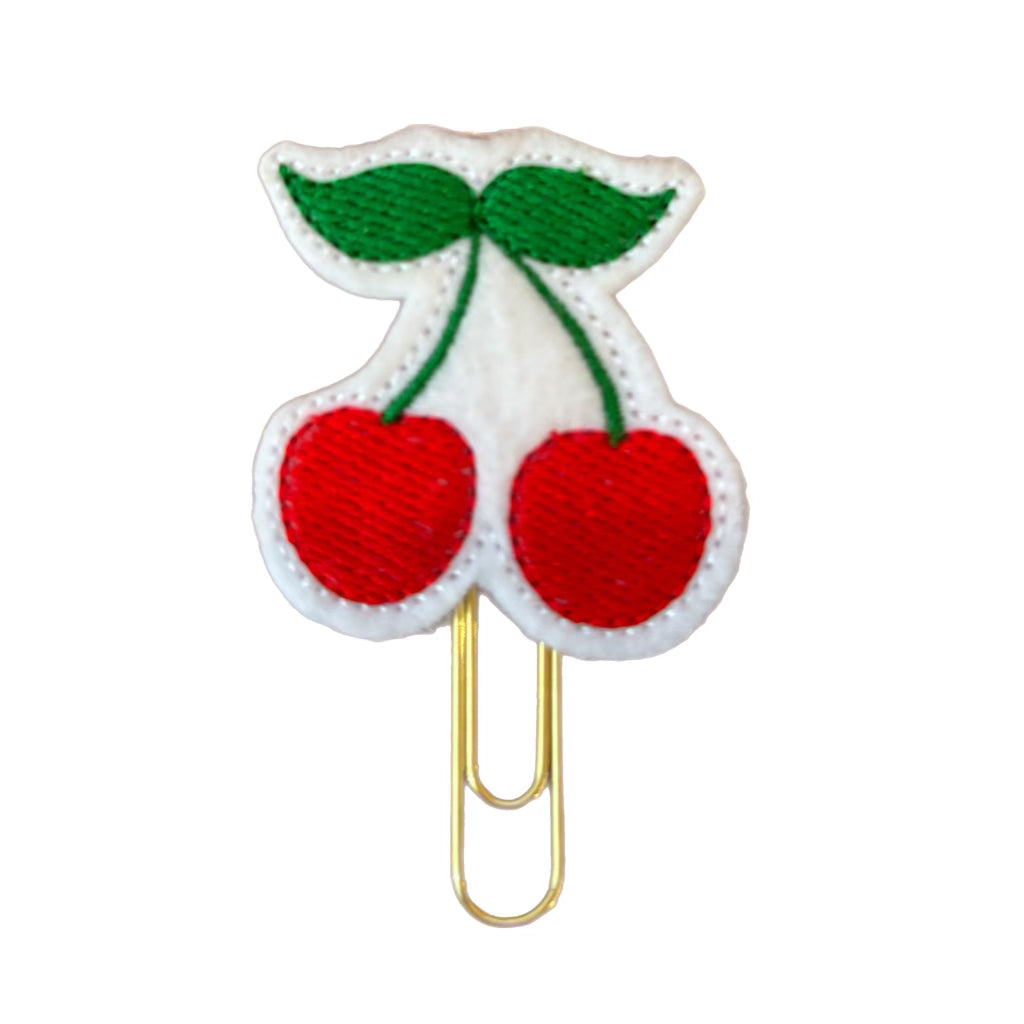 a set of embroidered cherries are attached to a gold toned paper clip , making Clip Chicks novelty paper clip great as a bookmark or planner clip.