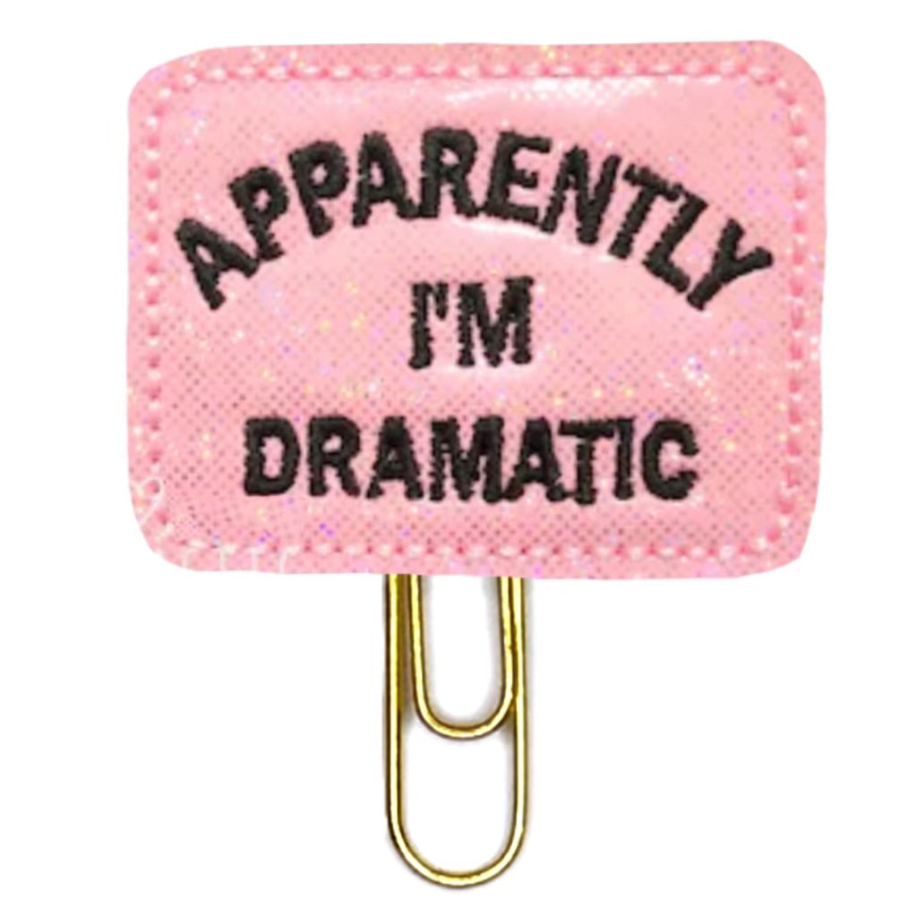 A novelty paper clip that reads "Apparently I'm Dramatic" is shown in a glittery pink with black embroidered words.