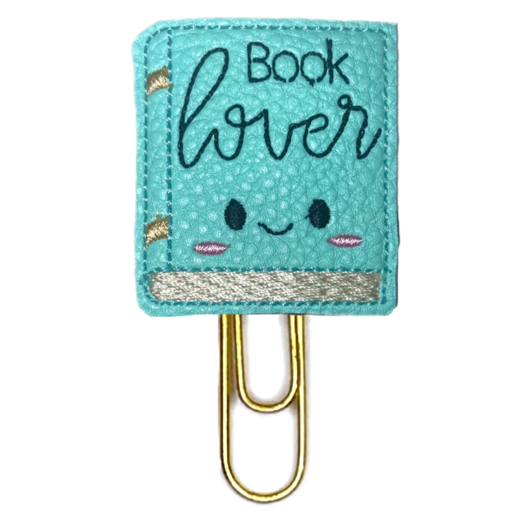 Book Lover novelty paper clip from Clip Chicks is a teal textured vinyl shaped like a book with eyes, and mouth embroidered on it along with the words, Book Lover.