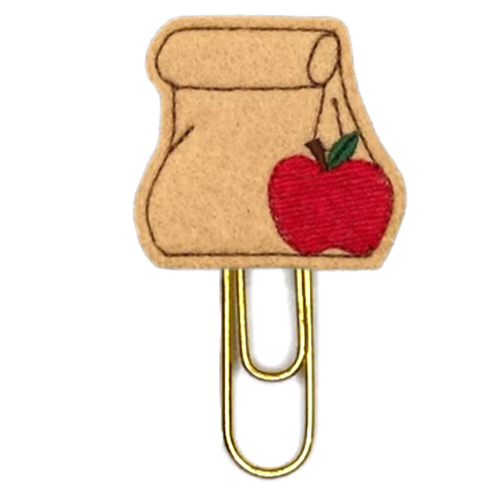 Brown Bag Lunch novelty paper clip from Clip Chicks is shaped out of felt to look like a lunch bag with a red apple embroidered on it, the paper clip is attached to the felt lunch bag.