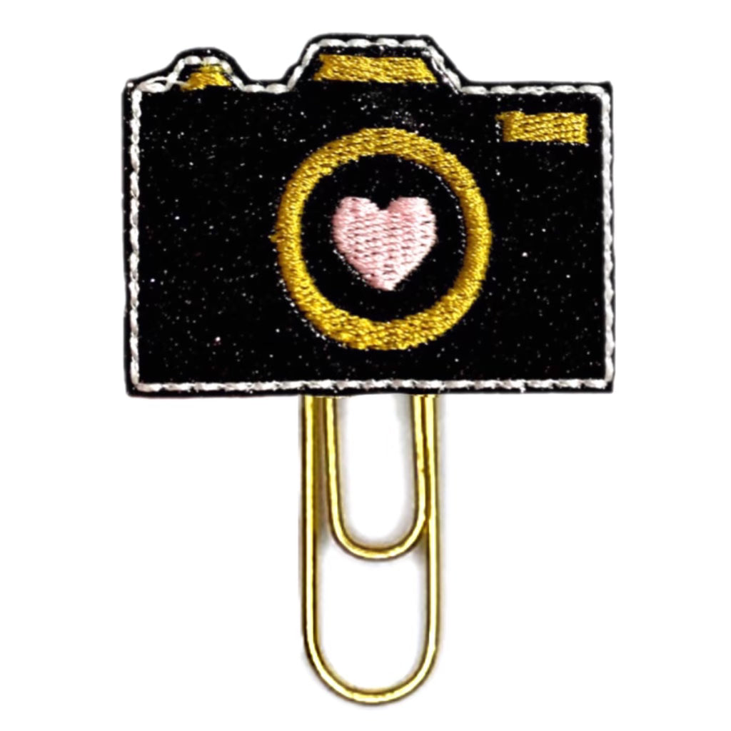 Black shimmery camera with a pink heart embroidered in pink in the center lens.