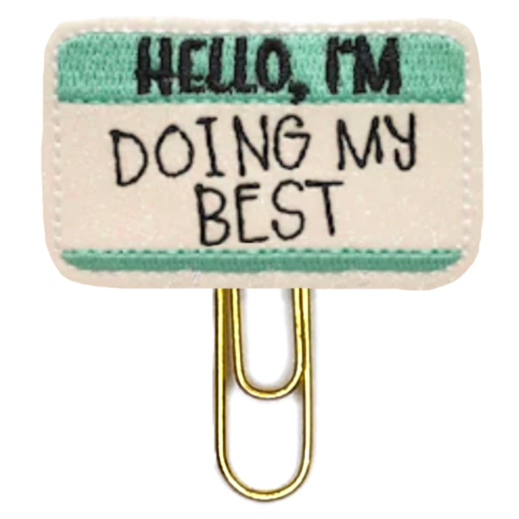 Hello, Im Doing My Best is embroidered onto  white shimmery vinyl with green and black thread, then attached to a paper clip.