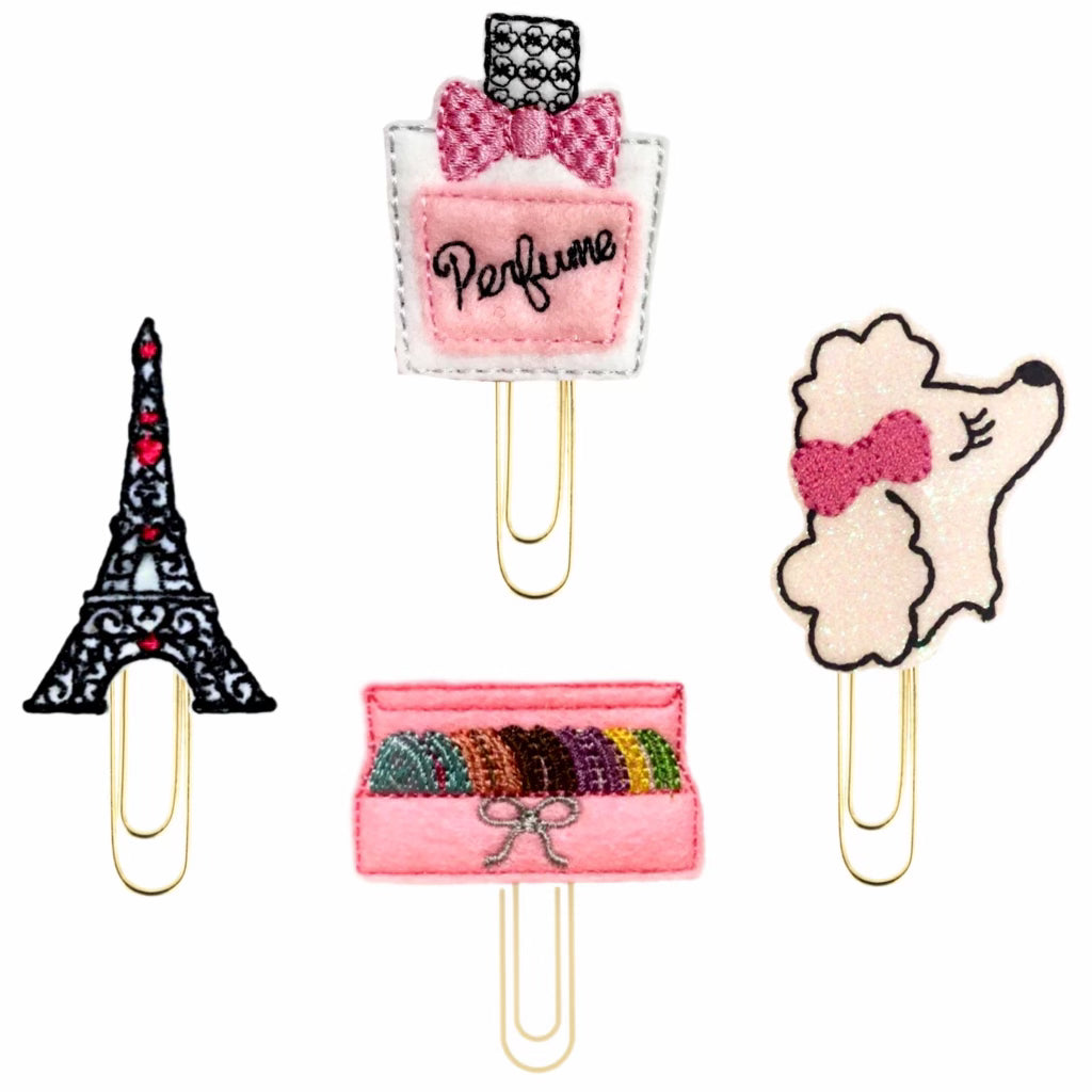 A set of four Parisian Style novelty paper clips include a bottle of perfume, a french poodle, a box of macaroons, and an Eiffel Tower paper clip.