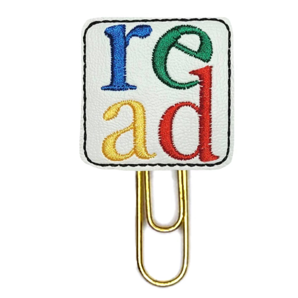 Read novelty paper clip from Clip Chicks is white vinyl with READ embroidered on it in red, green, blue and yellow thread and attached to a paper clip.