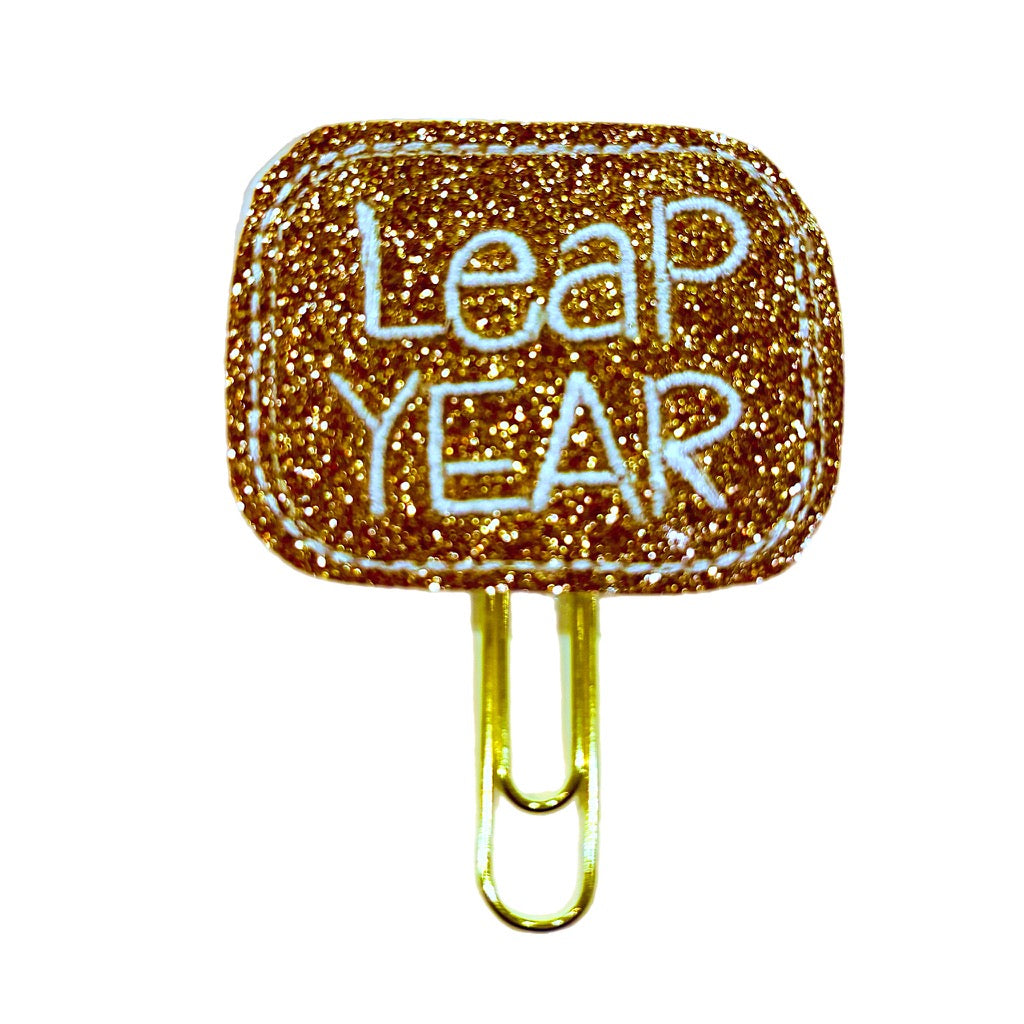 Rose gold shimmery feltie with white embroidered Leap Year on it attached to a paper clip made by Clip Chicks to be used as a planner clip, bookmark or desk accessory.